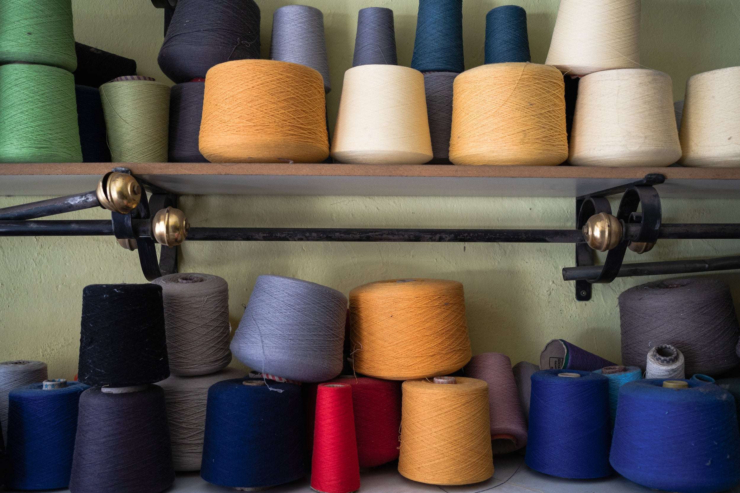Bunte Garnkegel auf Regalen, dicht aneinandergereiht, in Gelb, Blau, Rot, Grün, Schwarz, Grau, verschiedene Größen